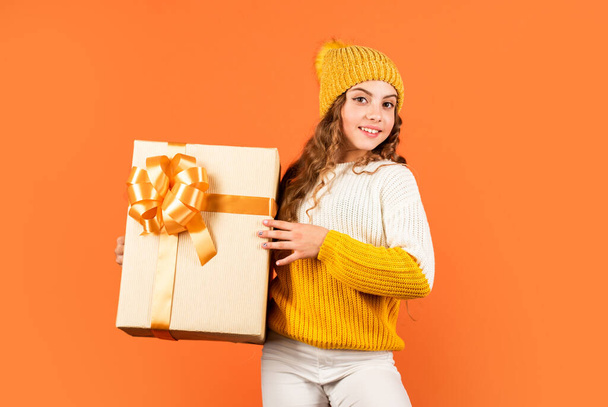 Birthday tradition. Fashionable little girl wear knitted hat and sweater. Birthday surprise. Pretty teen makeup face curly hairstyle. Kid hold present box. Shopping mall. Birthday celebration idea - Foto, afbeelding