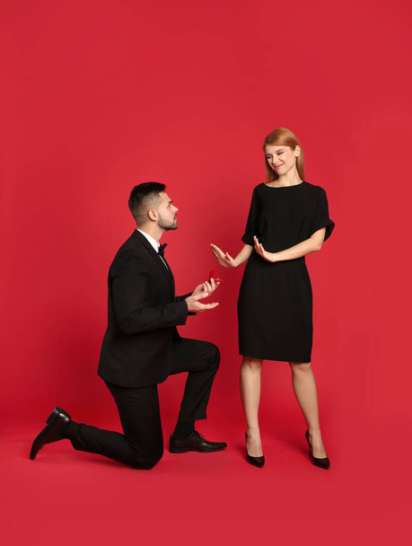 Young woman rejecting engagement ring from boyfriend on red background - Photo, image