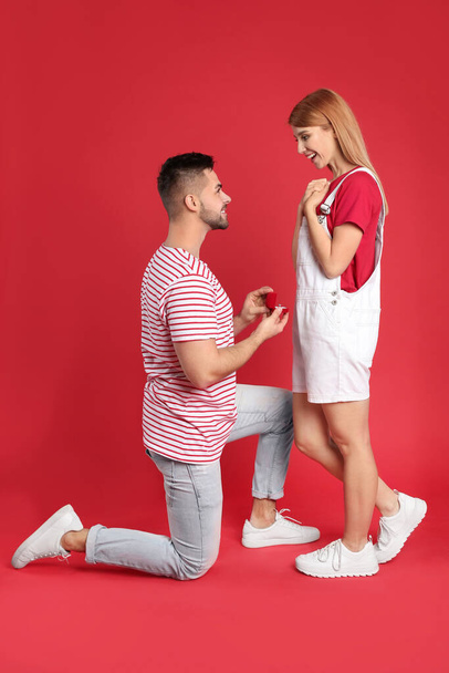 Man with engagement ring making marriage proposal to girlfriend on red background - Фото, изображение