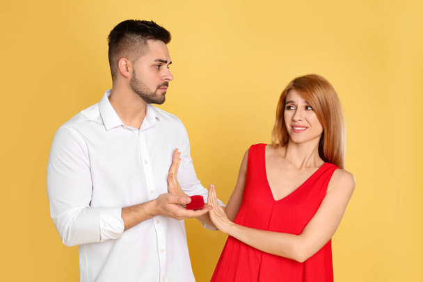 Young woman rejecting engagement ring from boyfriend on yellow background - Фото, зображення