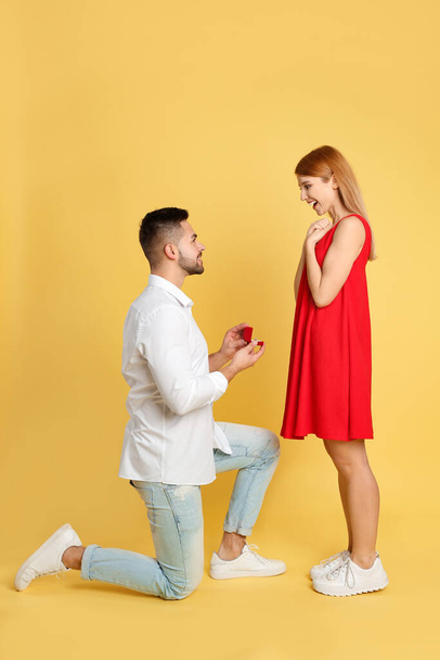 Man with engagement ring making marriage proposal to girlfriend on yellow background - Foto, immagini