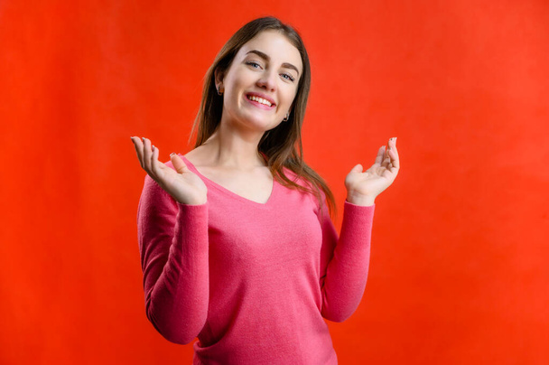 Photo on a red background of a pretty smiling woman in a pink sweater showing joy - Foto, Imagem