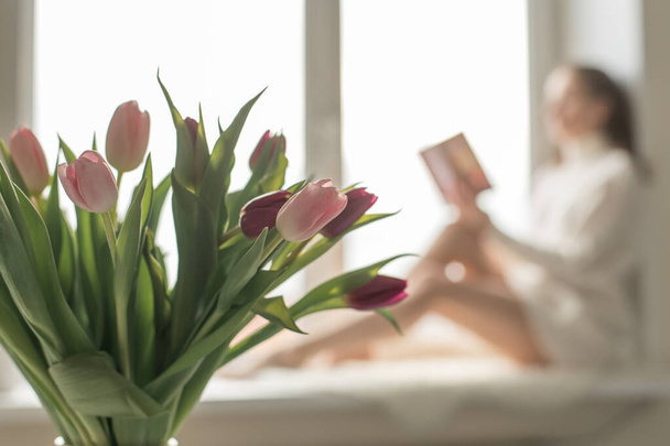 the scent of spring, a bouquet of pink tulips and the silhouette of a girl with a book. - Foto, Bild