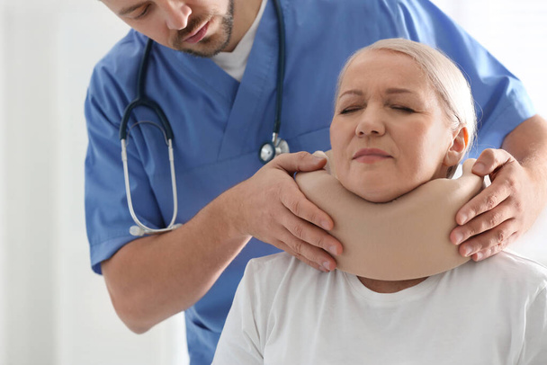 Orthopeed die cervicale kraag op de nek van de patiënt aanbrengt in de kliniek, close-up - Foto, afbeelding