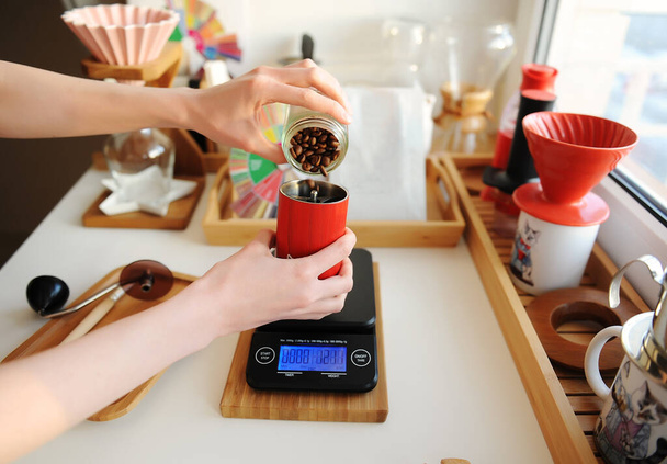 Alternatives Braustilleben. Kaffeebohnen auf elektronischer Ebene in eine rote Kaffeemühle gießen. Ästhetisches Konzept der dritten Welle - Foto, Bild