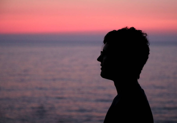 чорний профіль молодого чоловіка з змащеним волоссям і окулярами на морі з рожевим небом заходу сонця влітку
 - Фото, зображення