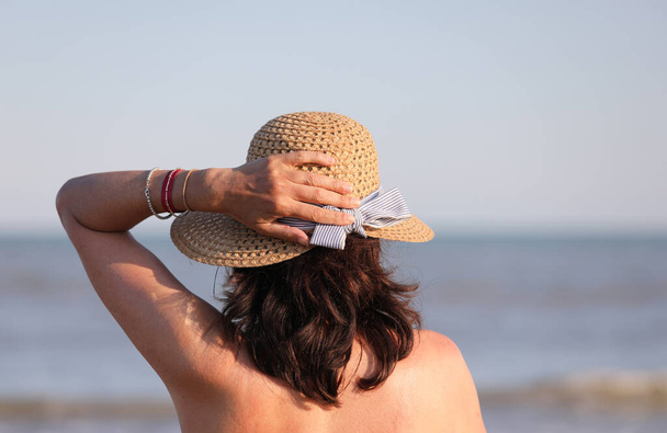 woman waiting with hand on the straw hat in summer by the sea - Photo, Image