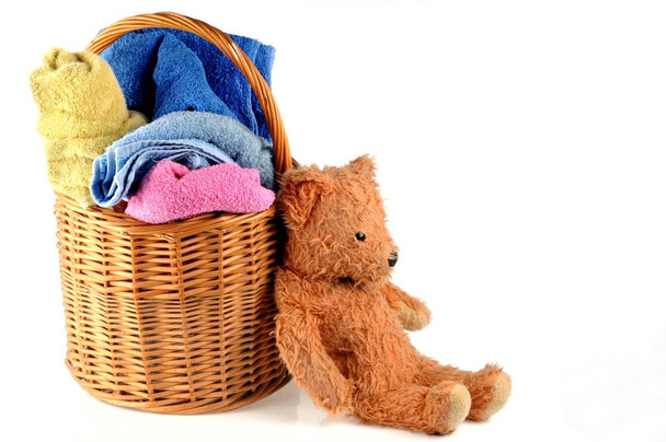 Koupelnové ručníky různých barev s plyšovým medvídkem v proutěném koši zblízka na bílém pozadí  - Fotografie, Obrázek