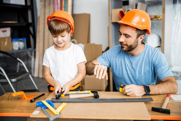 Smiling father teacing carpenter skills to son stock photo - Foto, afbeelding