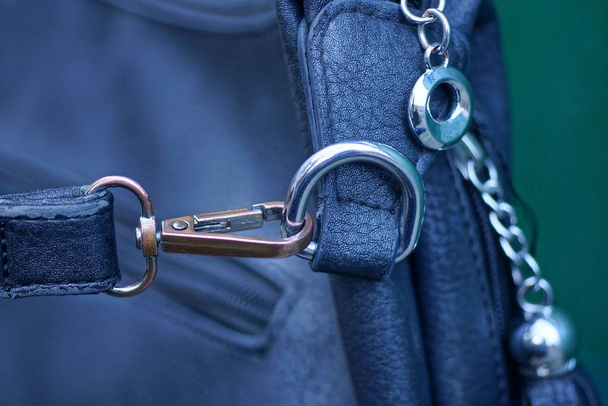 серый металлический карабин с кольцом и черной упряжкой на кожаной сумке
 - Фото, изображение