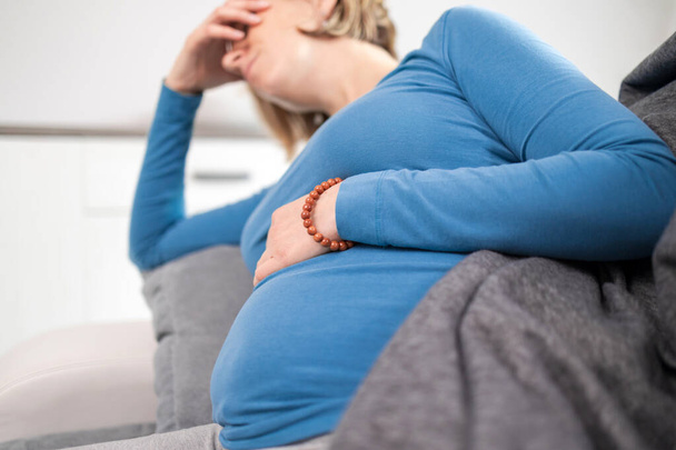 Pregnant tired exhausted woman with stomach and head issues at home on a couch, being sick. - Foto, imagen