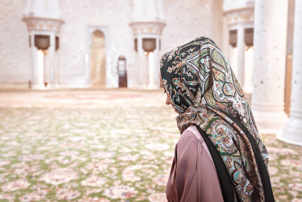 Frau im muslimischen Gebetsraum einer Moschee. Junge Frau mit Kopftuch. Traditioneller Teppich und arabische Architektur. Islam Religion und Tourismuskonzept. Rückseite weibliche Besucherin. - Foto, Bild
