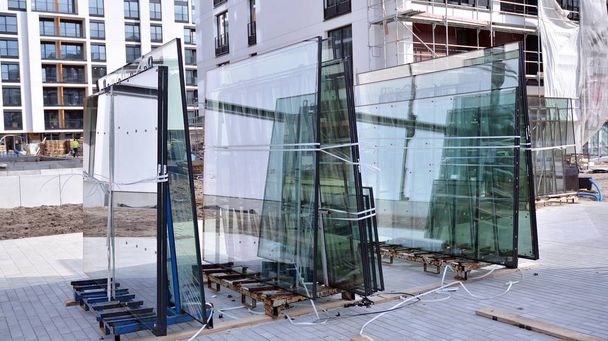 Des panneaux de verre dans le rack sont prêts à être soulevés et installés dans le bâtiment en construction. Fenêtre en verre double vitrage empilée et prête à être intégrée
. - Photo, image