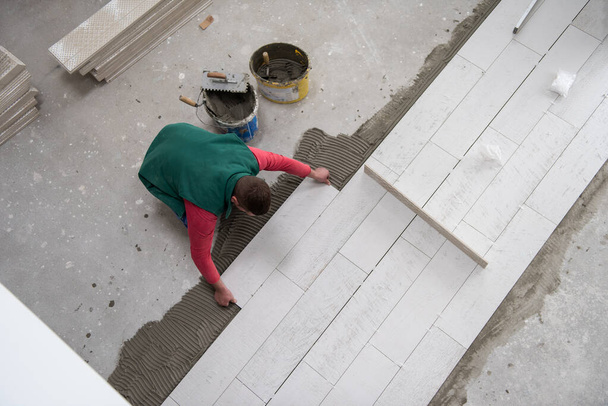 zkušený pracovník instalující keramické dřevo efekt dlaždice na podlaze Pracovník dělat laminátové podlahy na staveništi nového bytu - Fotografie, Obrázek