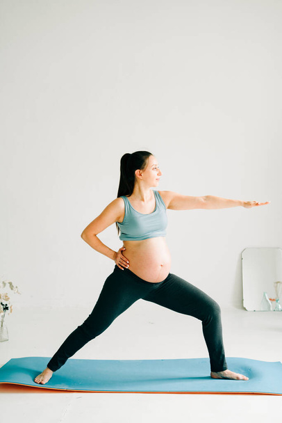 joven hermosa chica embarazada en ropa deportiva haciendo yoga, haciendo asana Virabhadasana-Guerrero Pose on the Mat
 - Foto, imagen