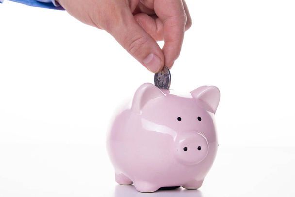 male hand puts a coin in a pink pig piggy bank on a white background. The concept of savings and savings, financial management - Φωτογραφία, εικόνα