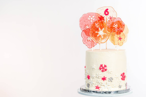 Tall round cake with Italian buttercream frosting decorated with fondant snowflakes and topped with large pink and white lollipops on a white background. - Photo, Image