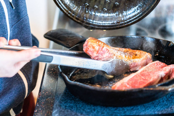 Frying New York strip steak in cast iron frying pan over the electric stove. - Фото, изображение
