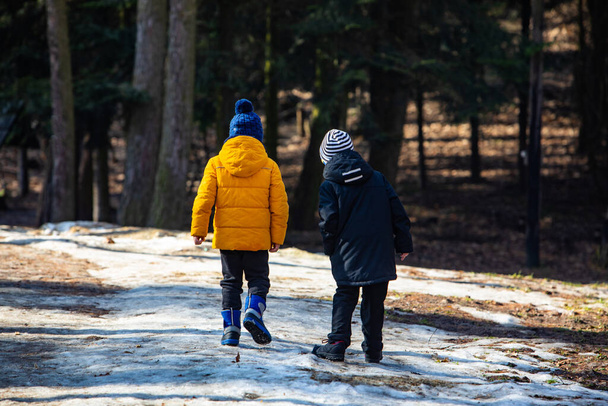 Két téli ruhás fiú sétál a havas park mellett. kilátás hátulról - Fotó, kép