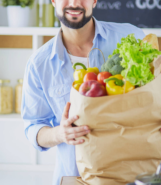 Man holding paper bag full of groceries on the kitchen background. Shopping and healthy food concept - Foto, Imagem