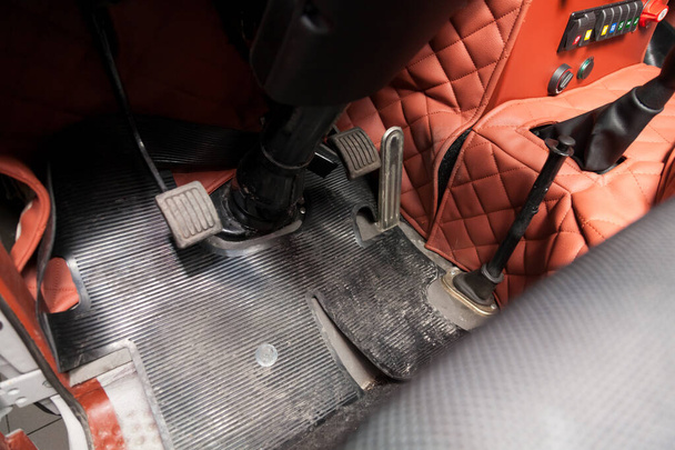 Verschmutzte Fußmatten aus schwarzem Gummi mit Gaspedalen und Bremsen in der Werkstatt für das Detaillierungsfahrzeug vor der Trockenreinigung. Auto-Service-Industrie. Innenraum des Lastwagens. - Foto, Bild