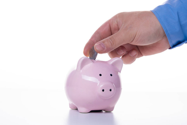männliche Hand steckt eine Münze in ein rosafarbenes Sparschwein auf weißem Hintergrund. das Konzept der Ersparnisse und Ersparnisse, Finanzmanagement - Foto, Bild