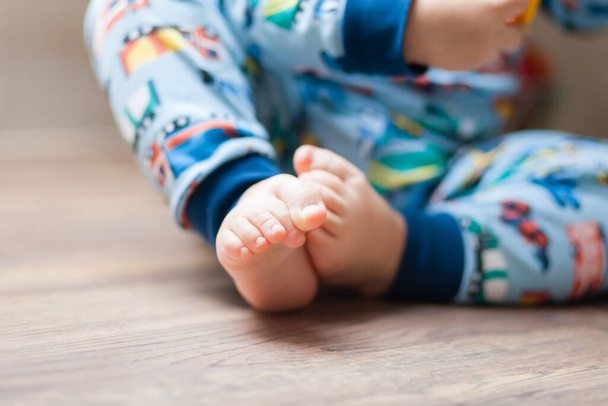 legs of a child with twisted fingers sitting on a wooden table in a blue pajamas with cars - Фото, зображення