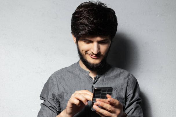 Portrait of self-confident young guy using smartphone. Bearded hipster man. Textured background of grey. - Photo, Image