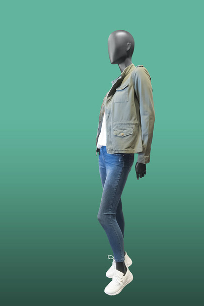Full length vrouwelijke mannequin dragen kaki jas en blauwe jeans, geïsoleerd op groene achtergrond. Geen merknamen of auteursrechtelijke objecten. - Foto, afbeelding