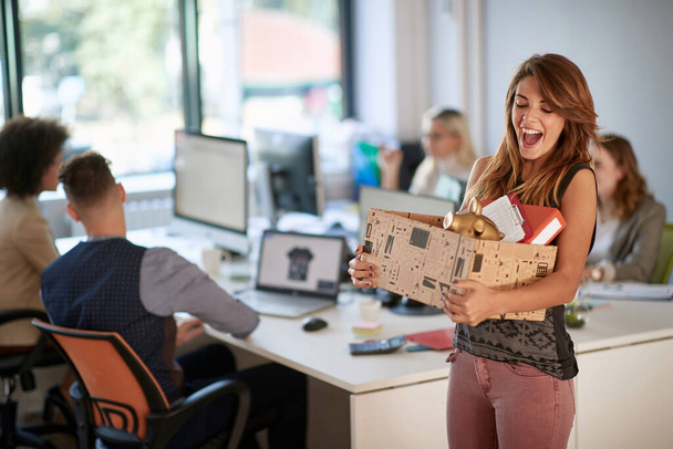 Szczęśliwa młoda kobieta trzymająca pudełko z rzeczami w biurze. Nowy początek w nowej pracy. - Zdjęcie, obraz