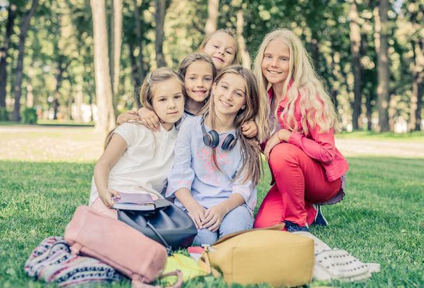 Ładne uśmiechnięte dziewczynki siedzą razem w parku - Zdjęcie, obraz