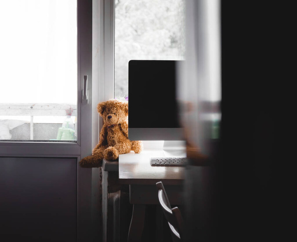自宅のオフィスでは、黄色いクマのぬいぐるみがコンピュータモニタの近くのテーブルの上に座っています。ぼかし、選択フォーカス、コピースペース. - 写真・画像