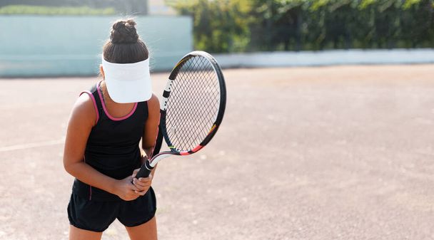 Портрет молодої дівчини-підлітка, з ракеткою в руці на тенісному корті, що чекає на службу. Носіння чорного тенісного костюма з білою шапочкою
. - Фото, зображення