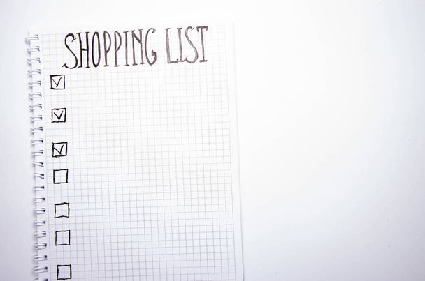 買い物リスト。白い背景に黒いペンの付いた正方形のノートブック。アイデア、メモ、計画、タスクを記録します。リストにはパン、牛乳、バナナが含まれています。コピースペース - 写真・画像