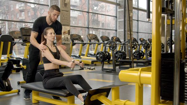 Young woman with instructor working out in gym by using rowing machine - Photo, Image