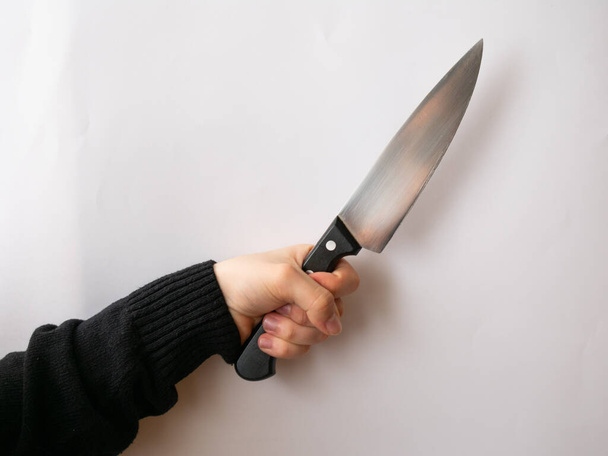 Caucasian hand on black sweater holding a cook knife, isolated on a white background, pointing to the right - Valokuva, kuva