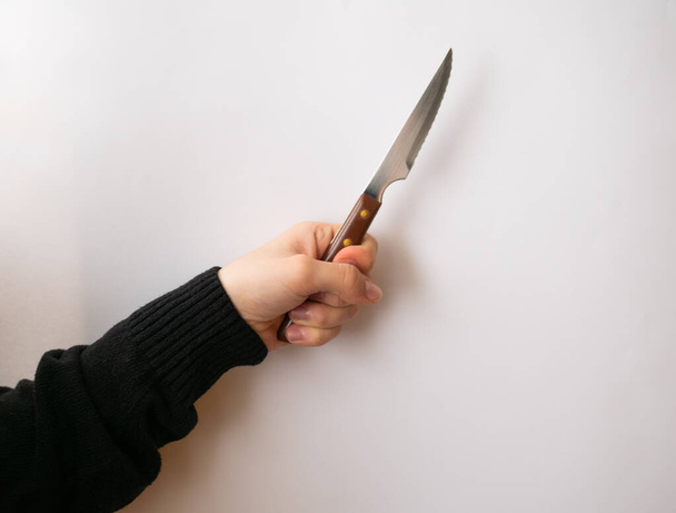 Caucasian hand on black sweater holding a meat knife, isolated on a white background, pointing to the right - Fotografie, Obrázek