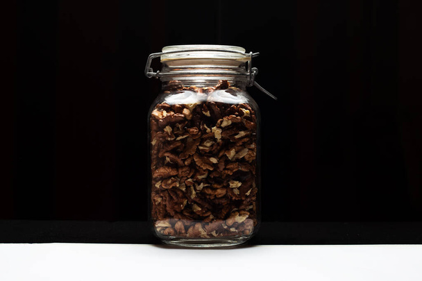 Close-up of glass jar with walnut, on black background. - Zdjęcie, obraz