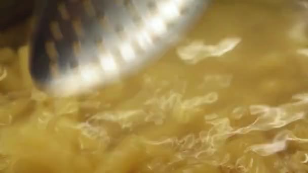 Metal spoon stirs pasta in boiling water. Closeup view - Filmagem, Vídeo