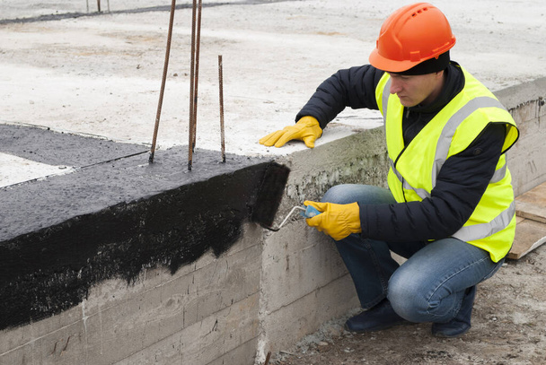 construction worker makes bituminous waterproofing of the foundation at the construction site - Photo, Image