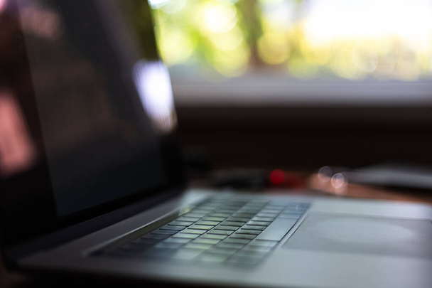 Κοντινό πλάνο του σύγχρονου laptop στο παρασκήνιο του παραθύρου. - Φωτογραφία, εικόνα