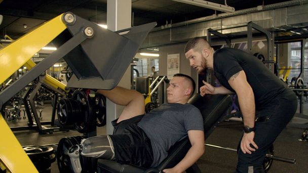 Jeune homme avec la jambe prothétique en utilisant la machine de presse de jambe dans la salle de gym
 - Photo, image