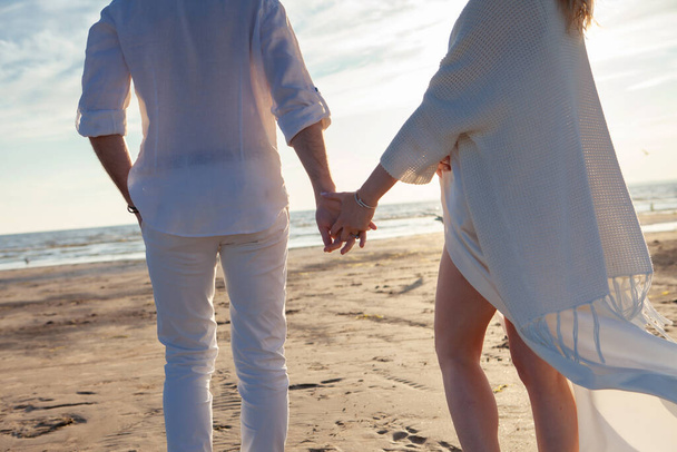 Aşk, sahilde romantizm. Genç güzel çift, kadın, erkek, beyaz gevşek uçan giysiler içinde, yürümek, deniz kıyısı boyunca. - Fotoğraf, Görsel