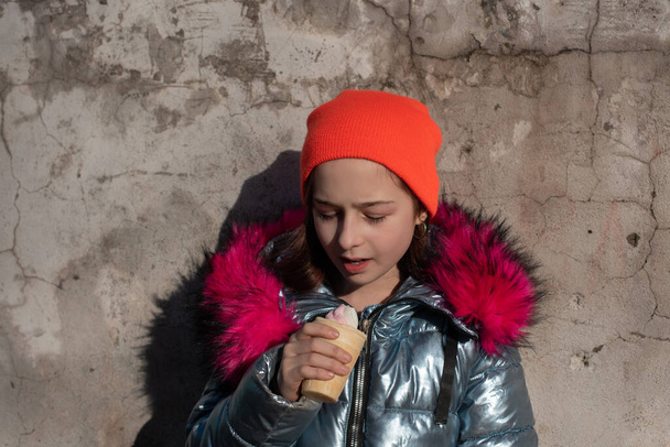 Kış Şapkalı Tatlı Mutlu Bebek Dondurma Yiyen Kız. Kışın dondurma yiyen kız. 9 yaşında bir kızın portresi. Sıcak bir kış gününde dışarıda dondurma yiyen liseli kız. 10 yıl. - Fotoğraf, Görsel