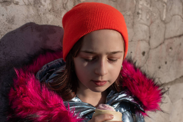 Leuk vrolijk peuter meisje in de winter hoed eten ijs. Meisje dat 's winters ijs eet. Portret van een meisje van 9 jaar oud. Schoolmeisje die buiten ijs eet op een warme zonnige winterdag. 10 jaar - Foto, afbeelding