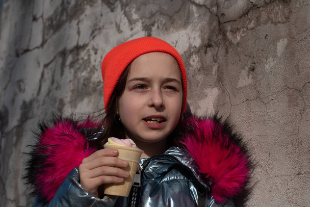 Kış Şapkalı Tatlı Mutlu Bebek Dondurma Yiyen Kız. Kışın dondurma yiyen kız. 9 yaşında bir kızın portresi. Sıcak bir kış gününde dışarıda dondurma yiyen liseli kız. 10 yıl. - Fotoğraf, Görsel