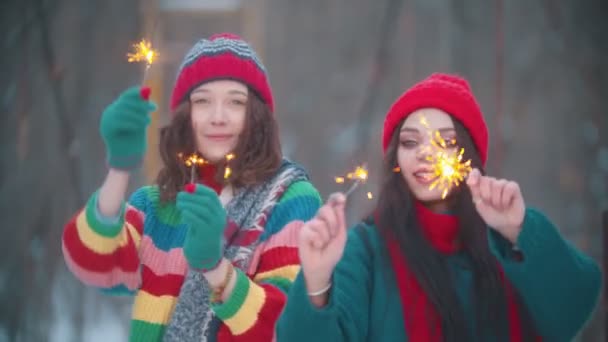 Δύο νεαρές χαμογελαστές γυναίκες χορεύουν έξω το χειμώνα με φωτισμένες σπίθες - Πλάνα, βίντεο
