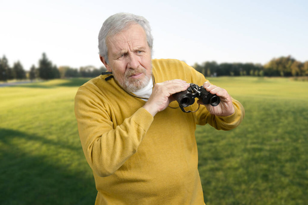 Old man with binoculars puzzled looking at sometning. - Foto, Bild