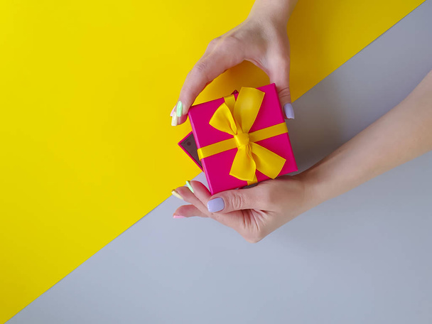 mani femminili che tengono una scatola regalo su uno sfondo colorato
 - Foto, immagini