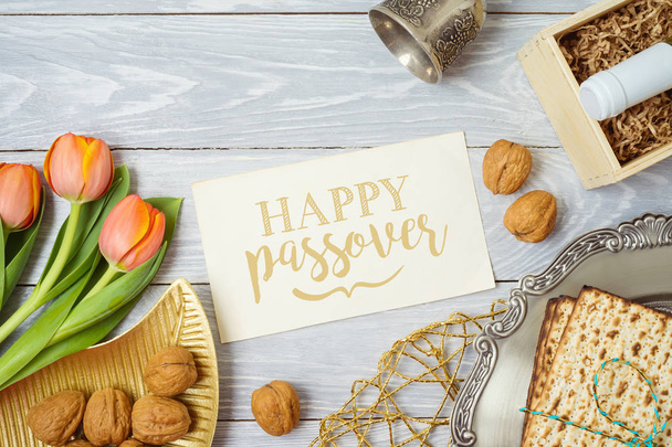 Jewish holiday Passover greeting card with matzo, seder plate, wine and tulip flowers on wooden table. Top view from above. - Photo, Image
